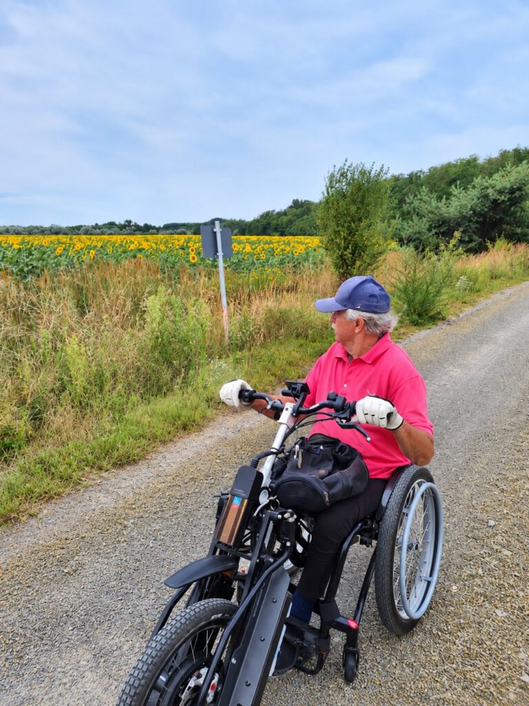 Wolfgang Steffan mit Handbike auf einem Feldweg am Sonnenblumenfeld